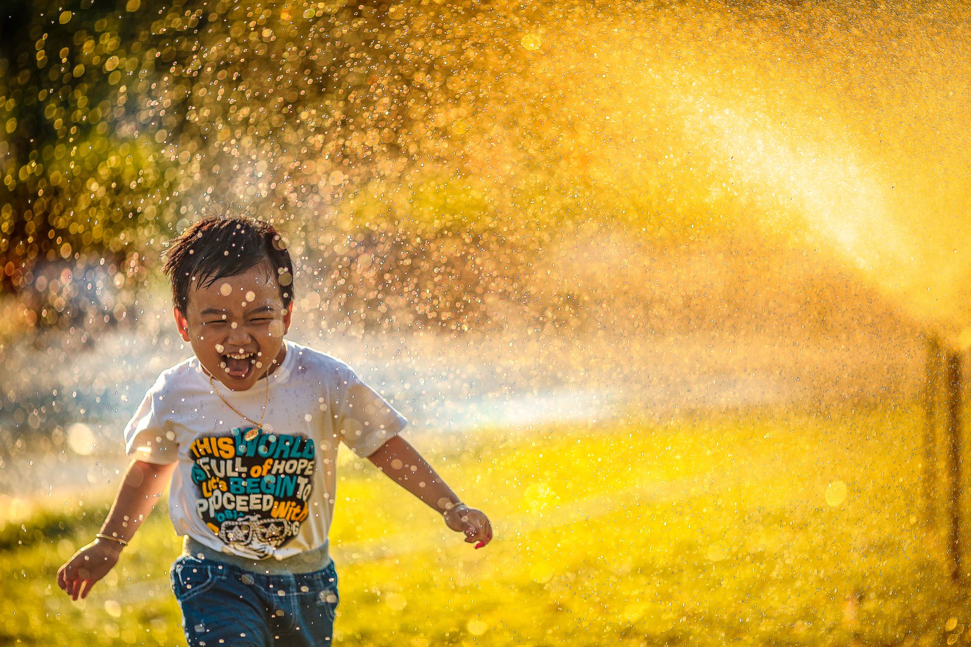 lifestyle photography shot of a little boy running through a sprinkler with a huge smile